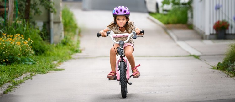 young girl in a purple helmet riding a bike 