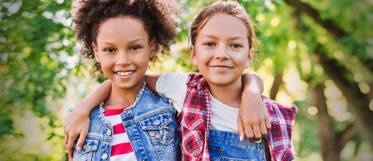 two respectful grade-school age girls in a park standing with their arms around each others shoulders