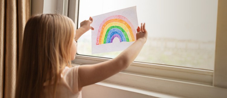 girl sheltering in place with rainbow in the window